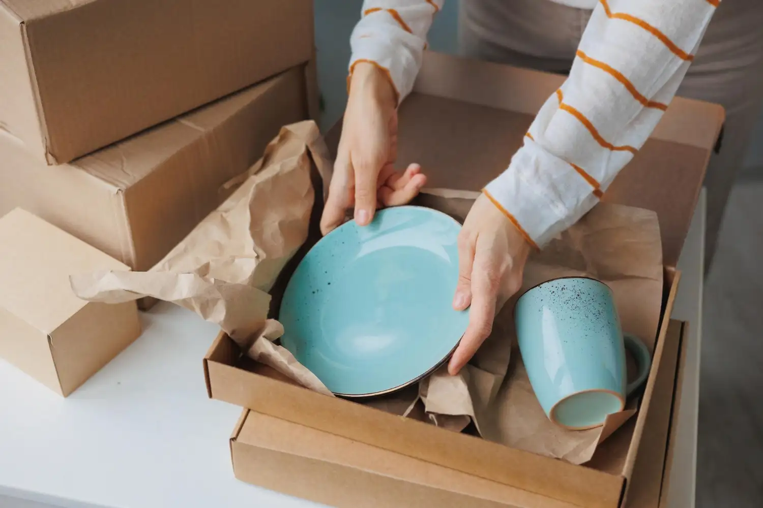 Türkise Keramikschüssel und Tasse werden mit Packpapier im Umzugskarton verstaut