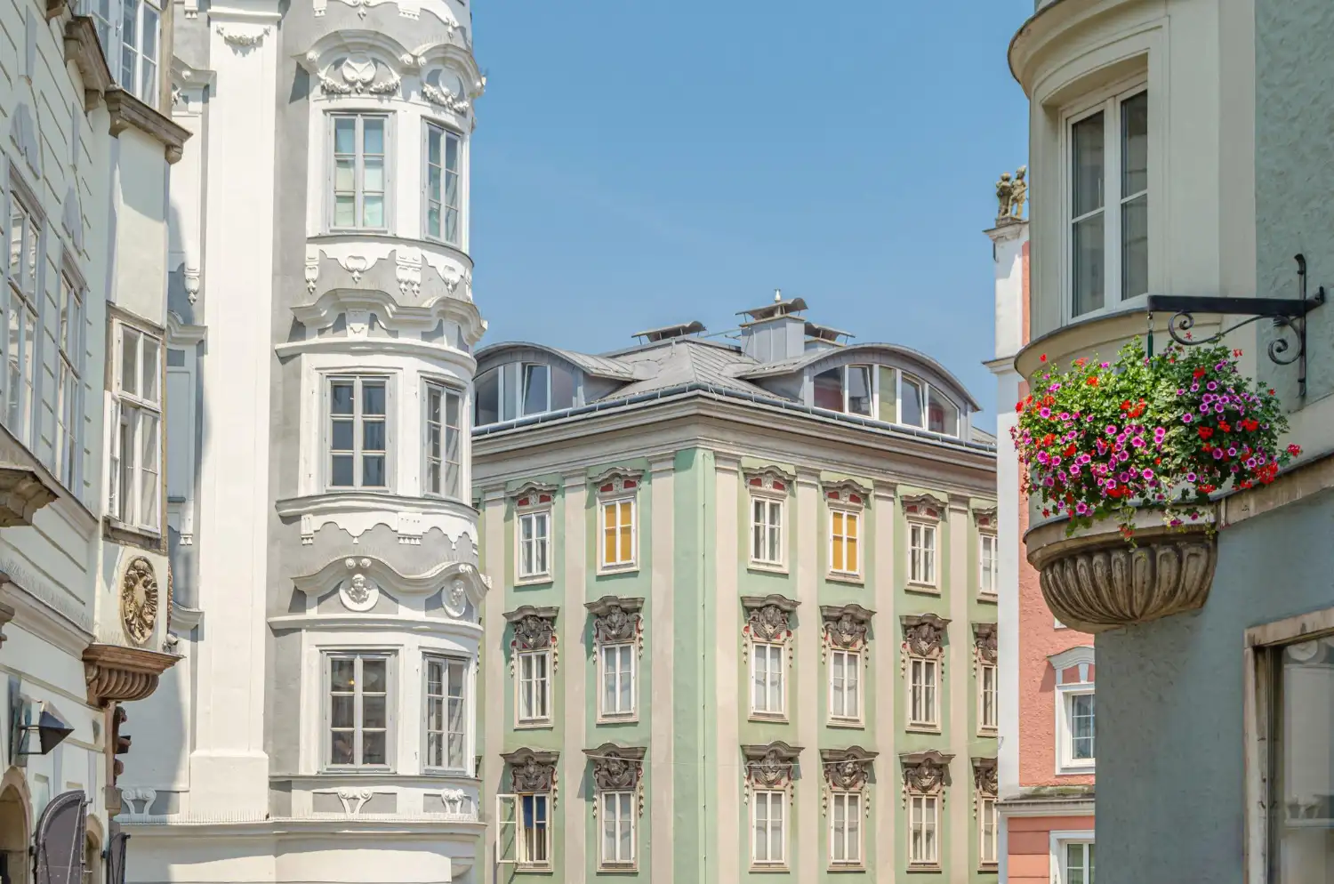 Barocke Altstadtfassaden in Linz mit Blumenschmuck und Erker unter blauem Himmel