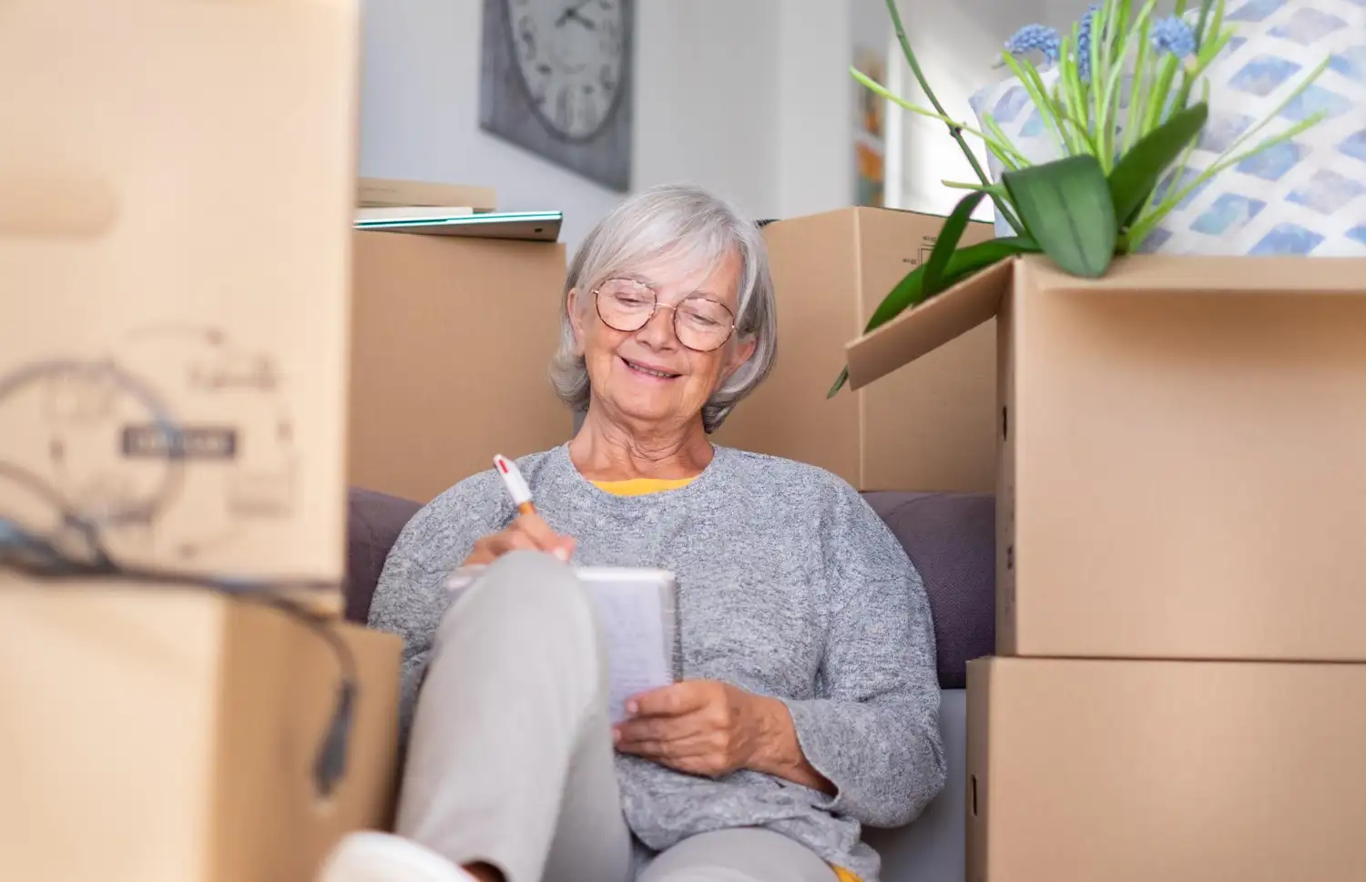 Seniorin plant ihren Umzug ins Pflegeheim und schreibt eine Checkliste zwischen Umzugskartons