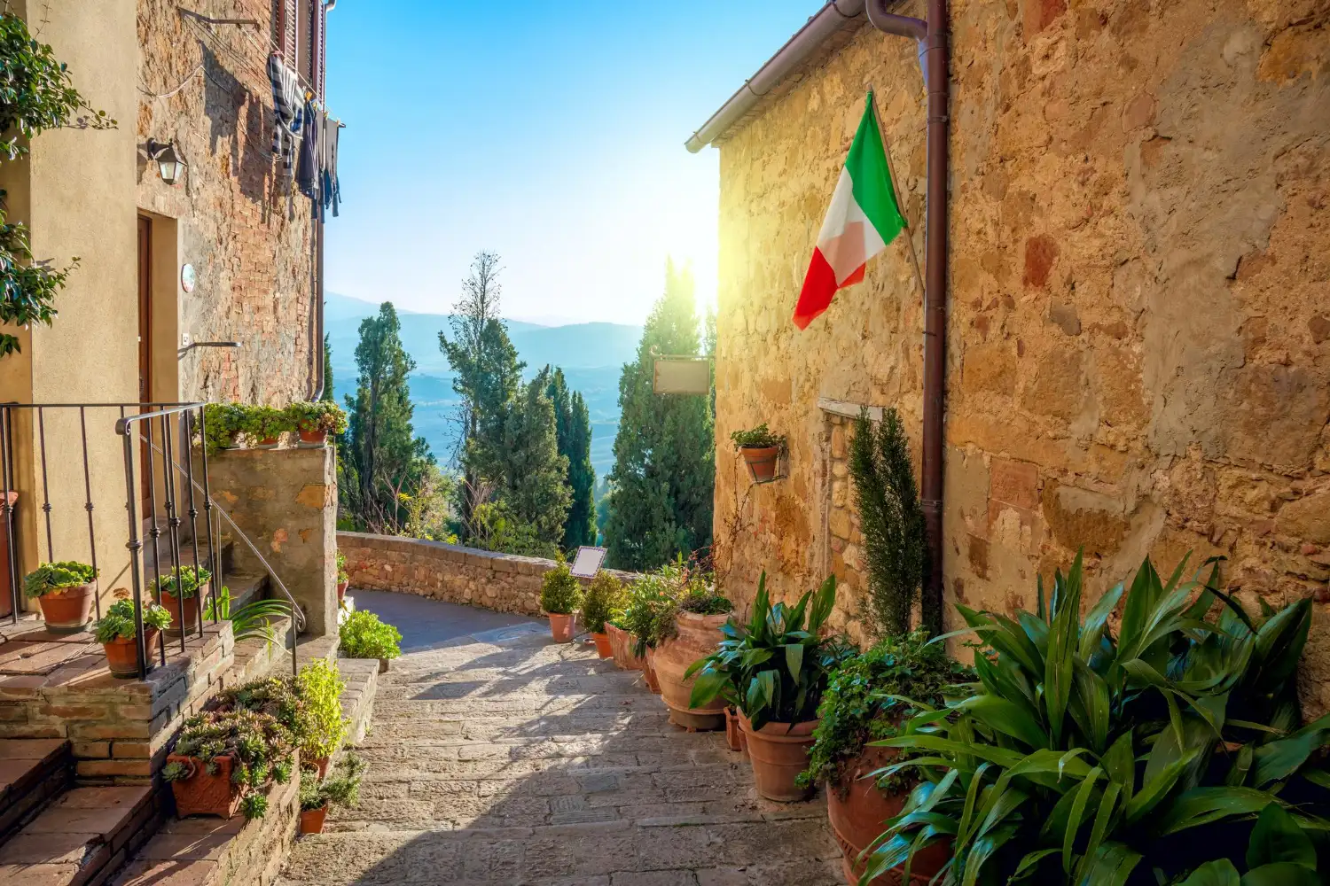 Sonnige Toskana-Gasse mit italienischer Flagge und Terrakotta-Töpfen beim Umzug Italien